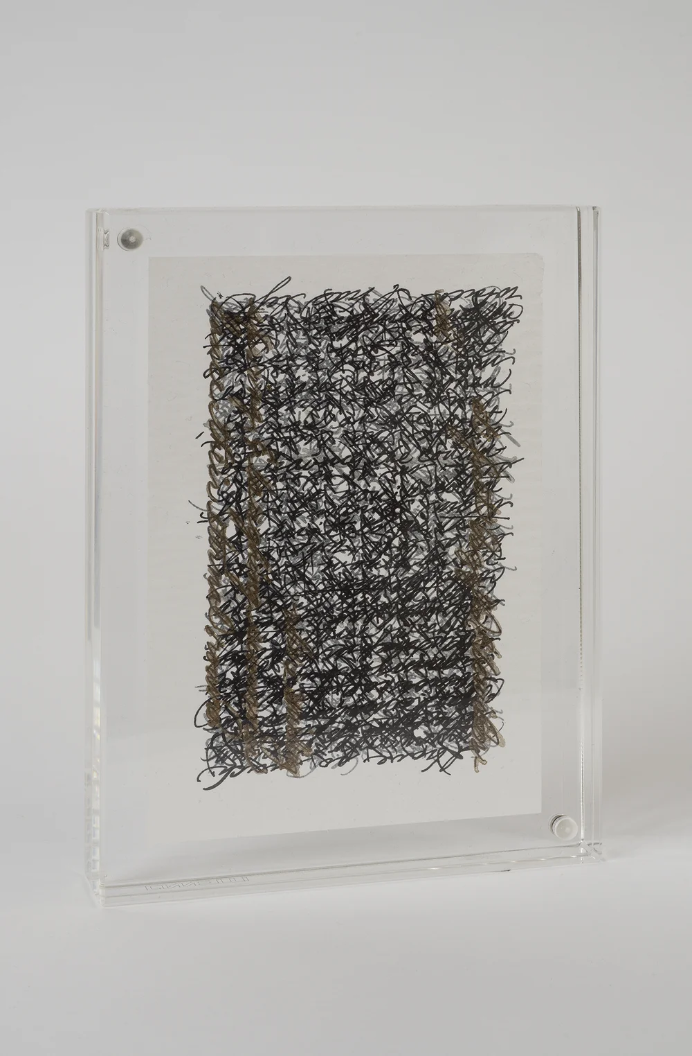 Close-up of a framed abstract sketch with dense black scribbles and thread-like brown vertical lines, displayed in a clean neutral setting